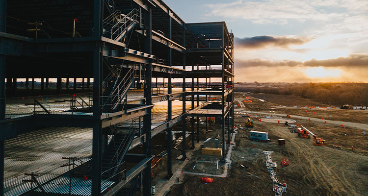 Amazon Fulfillment Center under construction, likely depicting the steel structure of a large warehouse facility at sunset.