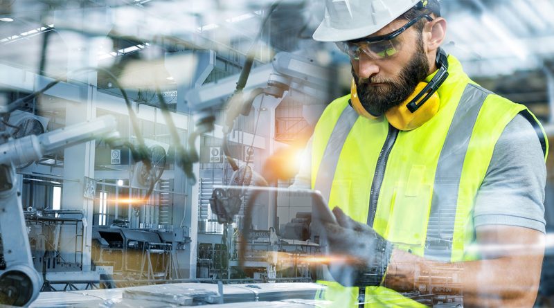 Construction worker using a digital tablet on-site in a modern industrial facility with robotic machinery in the background, representing advanced construction technology and project management tools.
