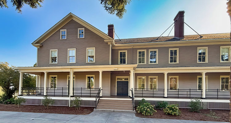 a two-story, L-shaped building with a wide porch that extends across the front.