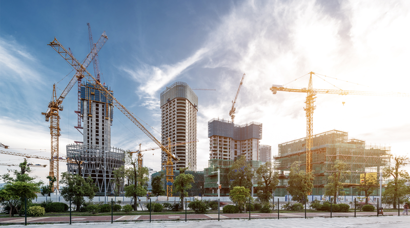 Urban construction site with multiple high-rise buildings under development and several tower cranes operating against a partly cloudy sky.