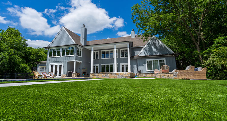 a lush, vibrant green lawn in front of a large, two-story house with grey siding