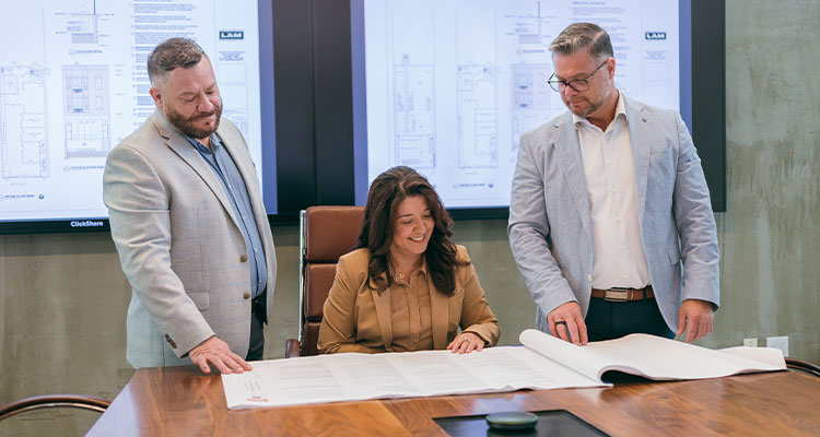 three people in a modern office environment reviewing architectural or construction plans on a large table