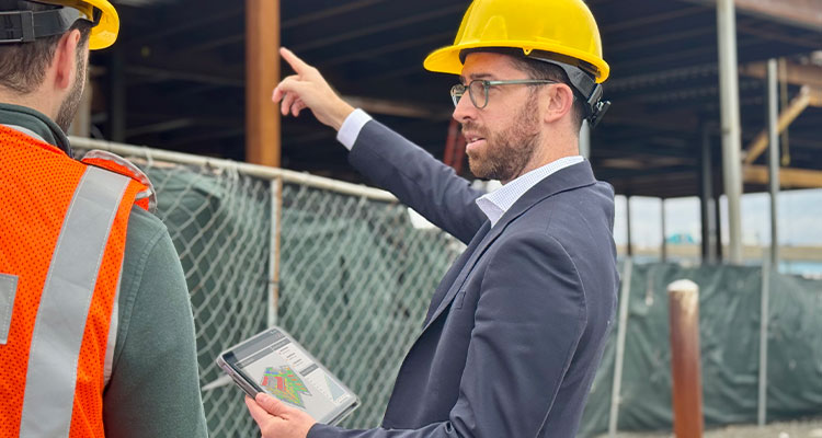 a man in a yellow hard hat and a suit is pointing at a construction site