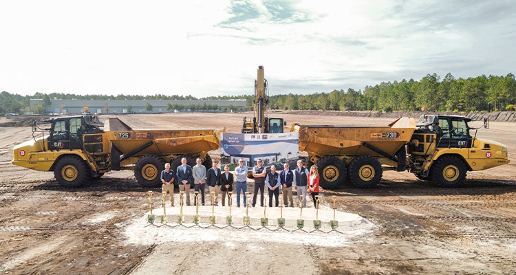 a groundbreaking ceremony featuring two Caterpillar 730 articulated dump trucks and an excavator.