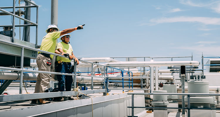 two people, wearing hard hats and safety glasses on an industrial platform